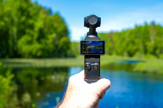 Rybinsk, Russia - June 05, 2026: DJI Osmo Pocket 3 gimbal camera in hand records calm river, green forest and blue sky with blurred summer background