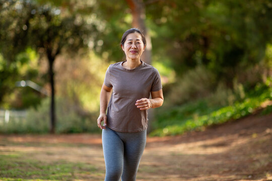 East Asian woman jogging through woodland trail