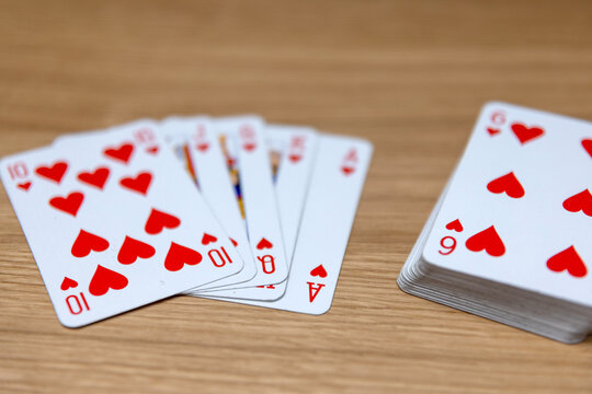 Hand holding a playing card &mdash; six of hearts, card deck on table, gameplay moment
