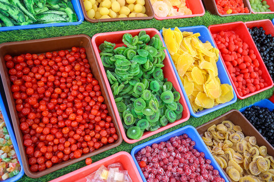 Side view of colorful dried and candied fruits, including kiwi, mango, cherries and assorted fruit snacks displayed in trays at a local market stall in Kashmir, India.