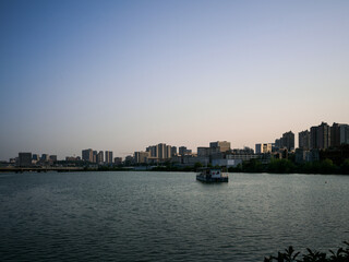 Fototapeta premium Small boat on calm lake water reflecting distant city skyline at evening twilight