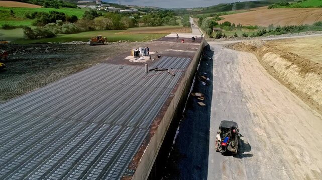 Aerial view of a highway bridge construction site with deck waterproofing, road base preparation, workers and machinery building modern transportation infrastructure.
