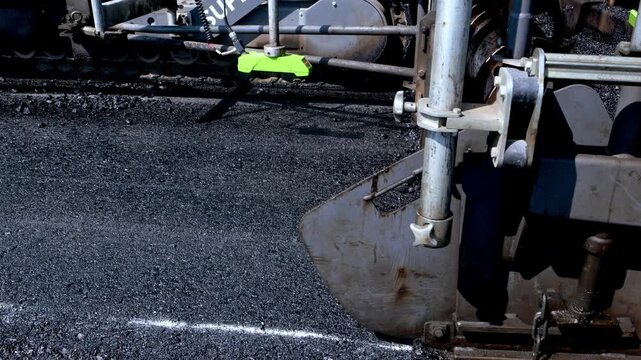 Close-up view of an asphalt paver spreading hot mix on a road construction site, showing fresh blacktop texture, machine details and highway paving process during infrastructure work.