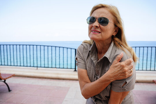Senior woman feeling shoulder pain by the sea