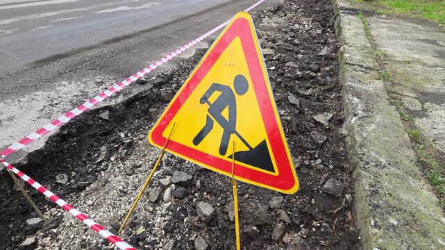 Rustic construction scene. Active roadwork with caution signs. Construction marker near excavation site. Temporary safety warning flag beside disturbed earth and repair tools