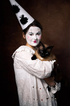 Mime performer holding Siamese cat, theatrical portrait with dramatic expression indoors