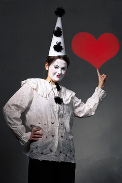 Playful mime clown posing with red heart, theatrical romantic studio portrait