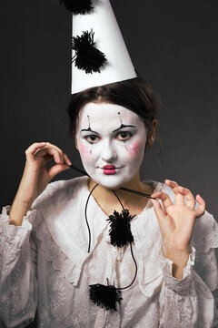 Woman in clown makeup pulling the elastic string of her party hat