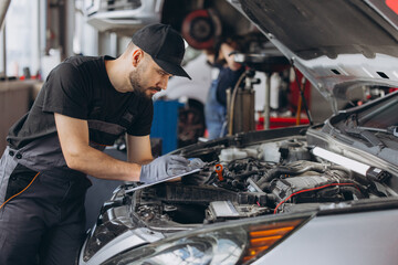 Mechanic performing car diagnostic and maintenance service, writing notes on clipboard in auto repair workshop © anatoliycherkas