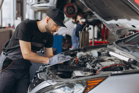 Mechanic performing car diagnostic and maintenance service, writing notes on clipboard in auto repair workshop