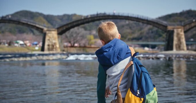 Boy with Backpack Looking at Arched Bridge over River In Japan - Medium, Rack Focus Shot