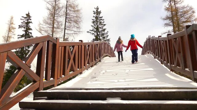 Two little beautiful girls walk on bridge near Strbske Pleso, is a favorite ski, tourist, and health resort in the High Tatras, Slovakia.