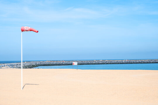 Blue sky, yellow sand on the beach and red white wind indicator - windsock.