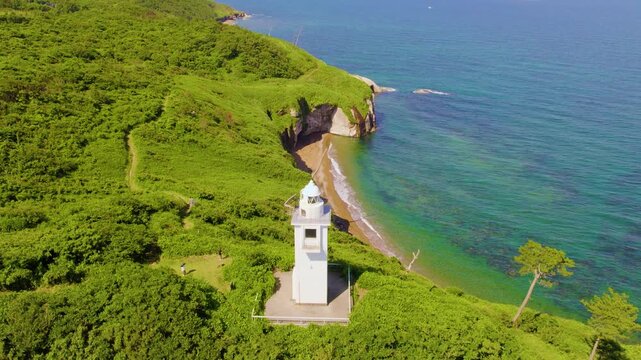 加佐の岬の断崖と灯台を見下ろすドローン俯瞰空撮 前進・ティルトダウン / Aerial drone pushing forward and tilting down over the white lighthouse and green cliffs of Cape Kasa