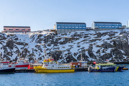 Fishing boats in the harbor below colorful houses on a snowy rocky hillside in Nuuk, Sermersooq, Greenland