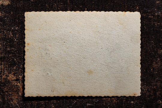 Blank vintage photo frame with wavy edges on dark background, closeup. Top view of an empty old textured paper card with scalloped edges isolated on dark brown grunge background copy space