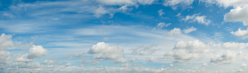 Fototapeta premium Vibrant blue sky dominates the scene. Soft white clouds drift across the horizon. Panoramic view captures open space and calmness. Bright daylight illuminates fluffy cloud formations