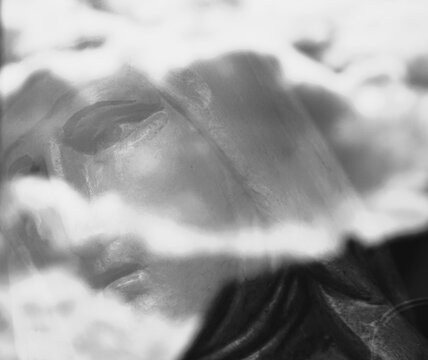 Abstraktes schwarz-wei&szlig; Motiv mit Abbild von Gesicht von Marien-Statue in wei&szlig;em Wolkenhimmel 
