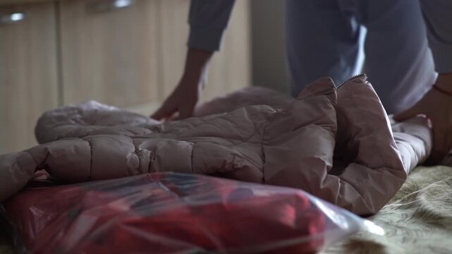 A teenager is busy sorting through and putting away winter clothes, closing the zipper on a down jacket to put them away in vacuum bags. High quality FullHD footage