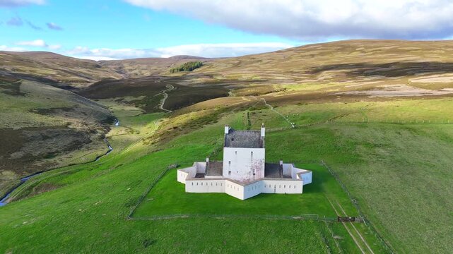 A cinematic drone shot approaches Corgarff Castle in Scotland, starting from distant rolling hills and gradually revealing its striking fortified structure.