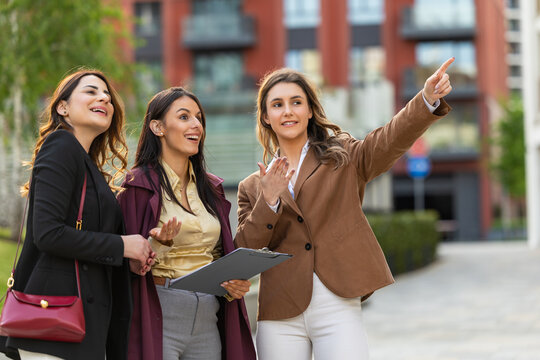 Businesswomen discussing property tour and pointing at urban development during professional meeting outdoors