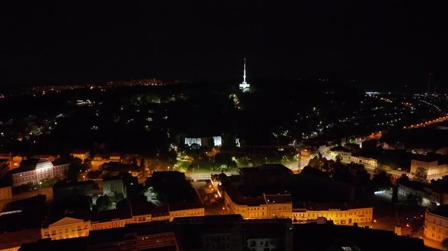 Night drone footage over Miskolc, Hungary, featuring the iconic Avas TV Tower rising above the city skyline. The video captures the illuminated tower, glowing streets, hillside neighborhoods