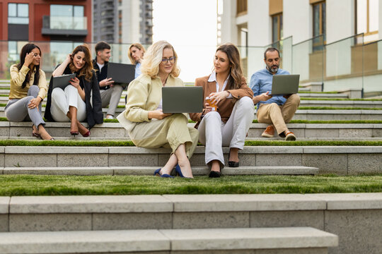 Group of professionals collaborating outdoors on laptops while sitting on urban steps