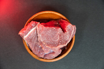Obraz premium Raw beef meat in a clay bowl on a dark background fresh red meat pieces for cooking, top view, closeup