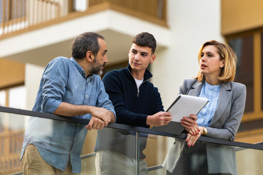 Three professionals discussing property plans on balcony using tablet during outdoor meeting