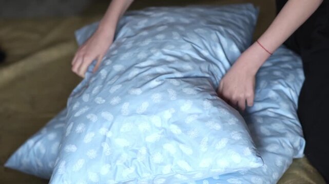 A teenage girl fluffs a new soft down pillow in her bedroom. The girl uses her hands to fluff the new pillows lying on the bed. High quality FullHD footage
