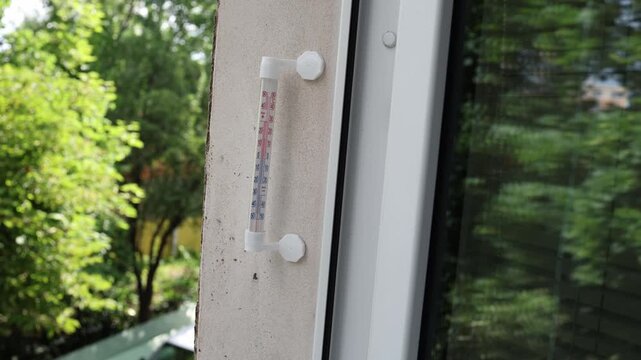 Close up of an outdoor thermometer mounted near a window displaying warm weather conditions summer heat seasonal climate and daily temperature monitoring