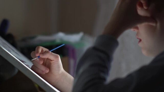 A teenager paints a paint-by-numbers picture on canvas with a brush. A boy dips a brush into paint and creates a creative drawing on a canvas. High quality FullHD footage