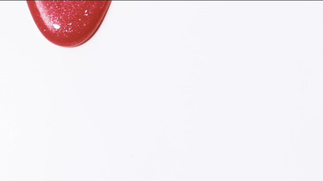 Close up of satisfying make up lipgloss flow. Red shimmering lip gloss texture pouring down on white background, Cosmetic product swatch background