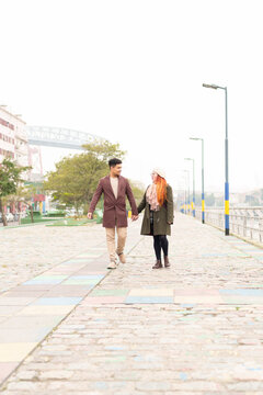 Young couple walking together on a promenade, holding hands and smiling