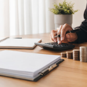 Business analyst working with financial data using calculator and documents on wooden desk in office with natural light and plant decor