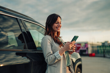 Businesswoman standing by car, typing on her mobile phone, smiling while using modern digital communication © Zamrznuti tonovi