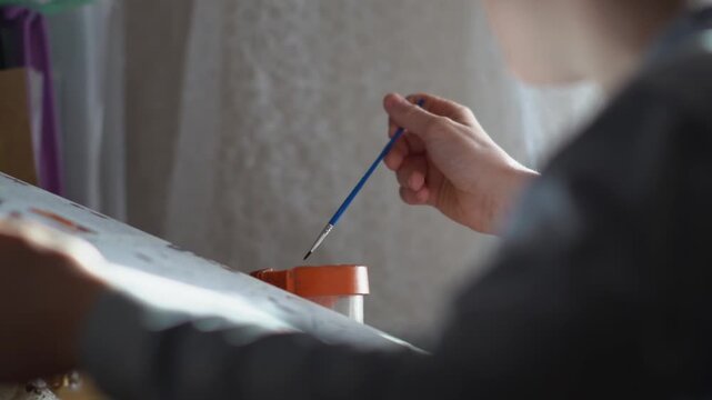 A teenager paints a paint-by-numbers picture on canvas with a brush. A boy dips a brush into paint and creates a creative drawing on a canvas. High quality FullHD footage