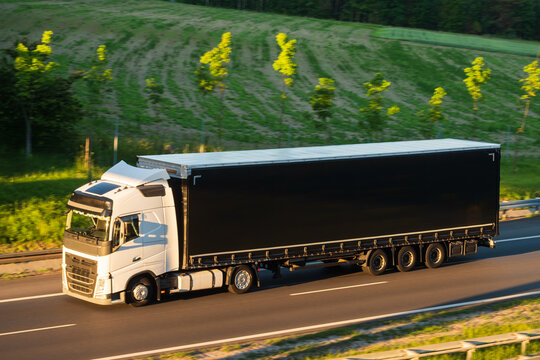 White Semi-Truck with Black Curtainside Trailer Driving on Highway Route, The Concept of Logistics