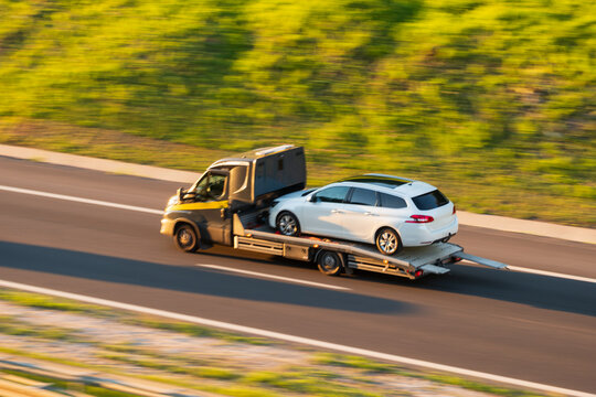 Flatbed Tow Truck Transporting White Station Wagon Car on Highway Route, The Concept of Roadside Assistance