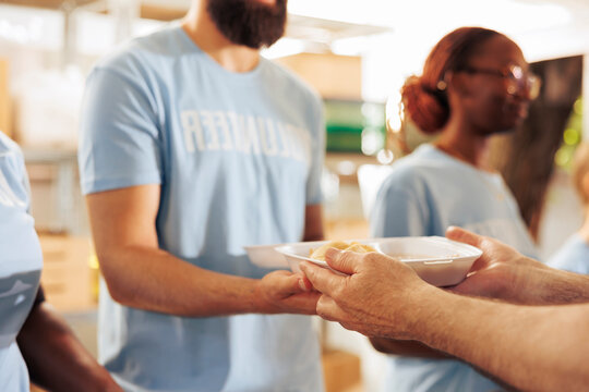 Close-up of a male charity worker handing out free food to the poor and homeless people. Volunteer holding a meal box to give to the hungry and less fortunate at an outdoor food bank.