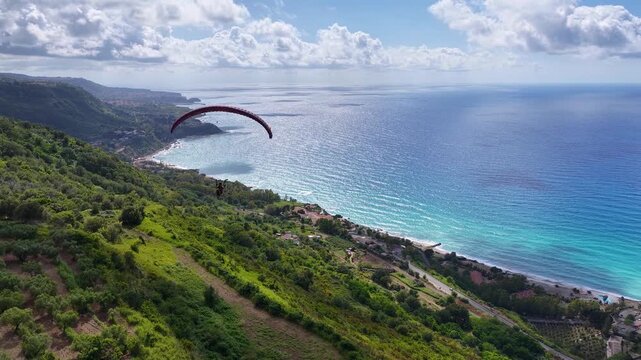 Tracking Aerial View of Paragliding Pacarhute Flying Above the sea and the coastline of Tropea, Italy. Summer Activity and Adrenaline Concept, Drone Shot