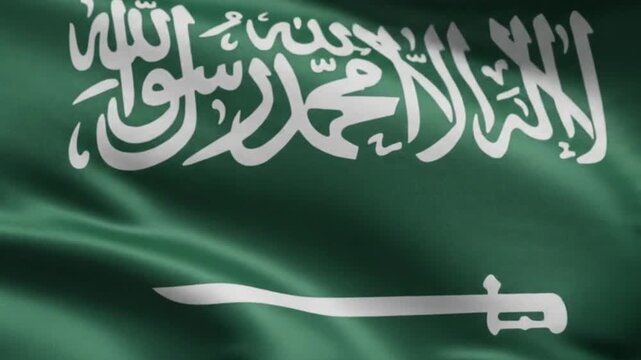 Waving flag of saudi arabia, close up view of the green fabric with white arabic script and sword symbol