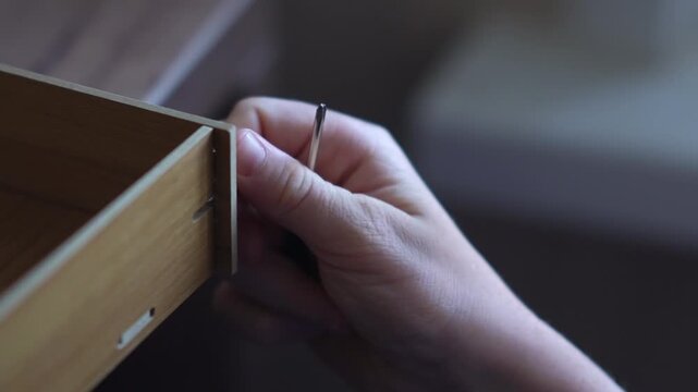 A teenager assembles a bookshelf. The child tries on the parts to assemble the furniture. Inserts a screw into the hole and tightens the parts
