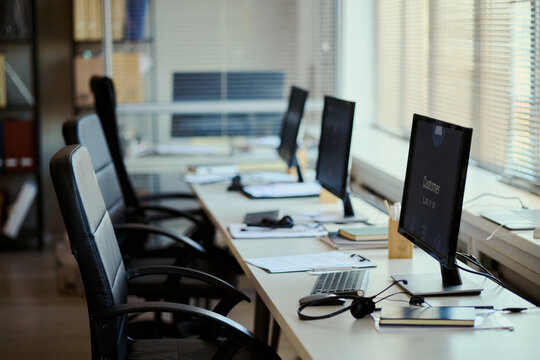 Wide shot of empty call center workstations displaying customer support software in team office, representing service operations and staffing needs. For contact center marketing