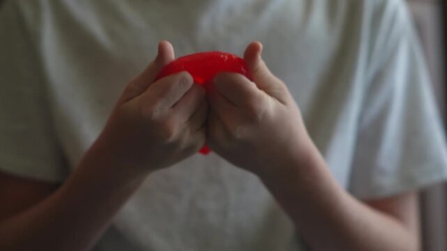 A child plays with homemade red slime. A fun sensory activity, stress relief, fine motor development, and a concept for educational content, toy stores, and home child development. 