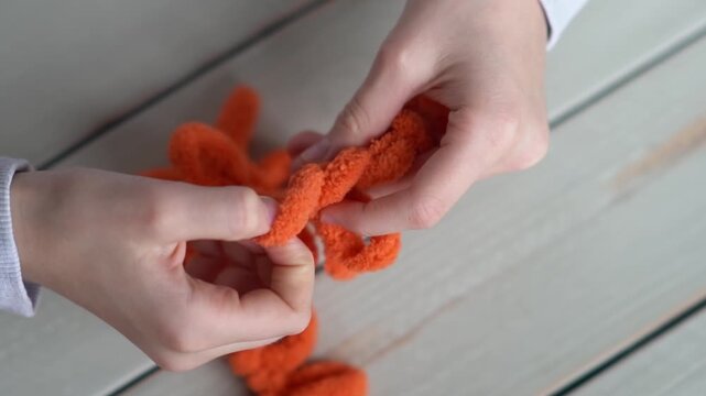 The fingers of a small child are knitting on orange yarn. Children's hobby. The girl sits holding a woolen thread in her hands.