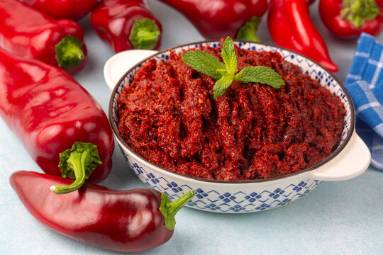 Traditional Turkish pepper paste salca garnished with a fresh mint leaf in a patterned bowl surrounded by red capia peppers
