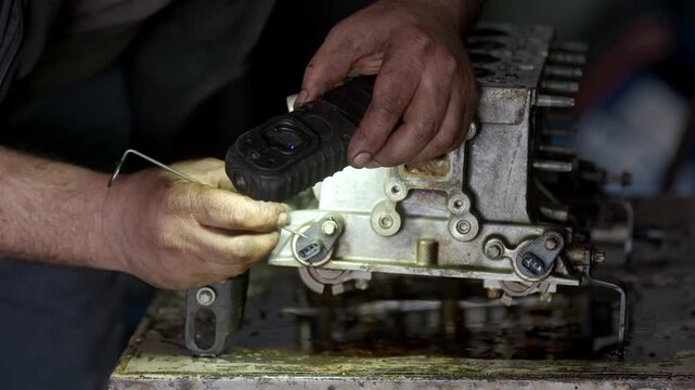 Close up shot of professional auto mechanic hands inspecting a vehicle engine cylinder head block with a flashlight in car service workshop. Technical automotive repair concept.