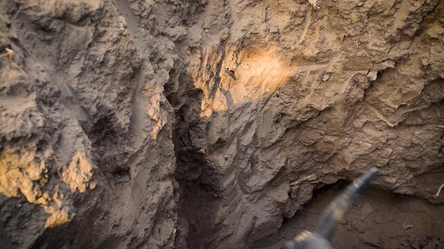 Young boy digging deep hole in dry ground at a construction site for excavation work, manual labor and physical effort