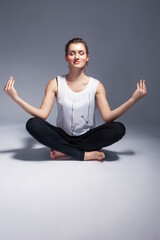 Obraz premium Active Winsome Sportive Caucasian Female During Yoga Stretching Exercise in Shirt and Black Tights Indoors Over White.